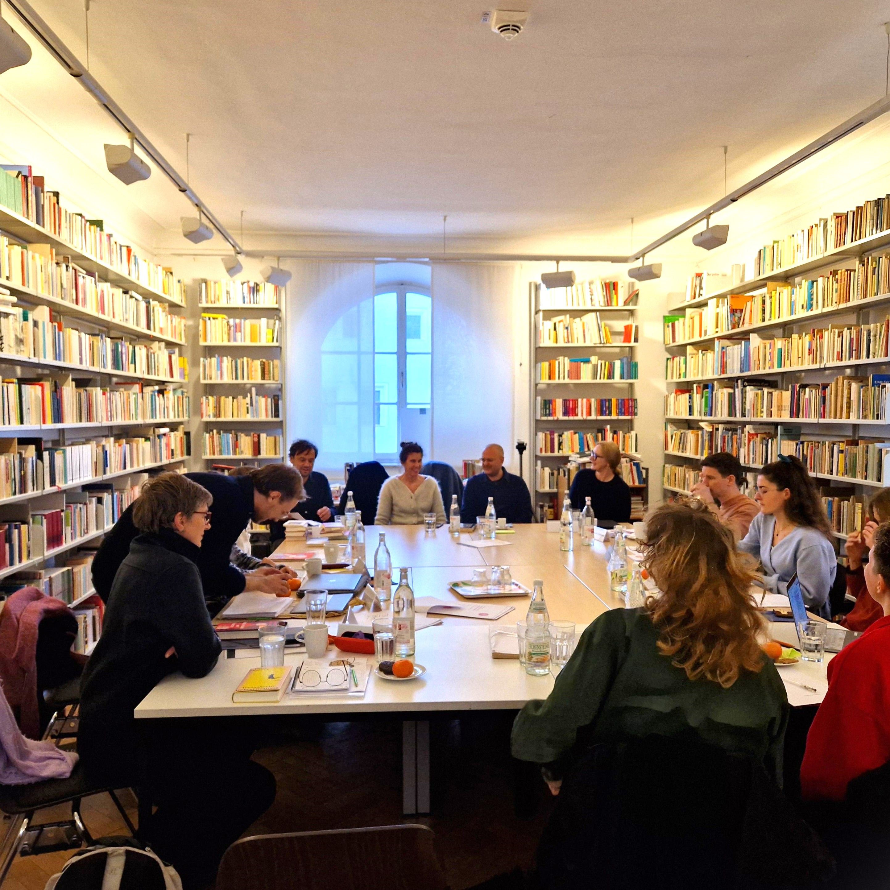 Männer und Frauen sitzen rund um einen großen Tisch in der Bibliothek des Literaturarchivs.
